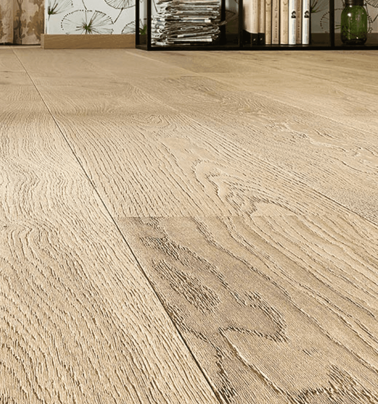 Close-up of textured light wood flooring in a room with a shelf holding books and magazines.