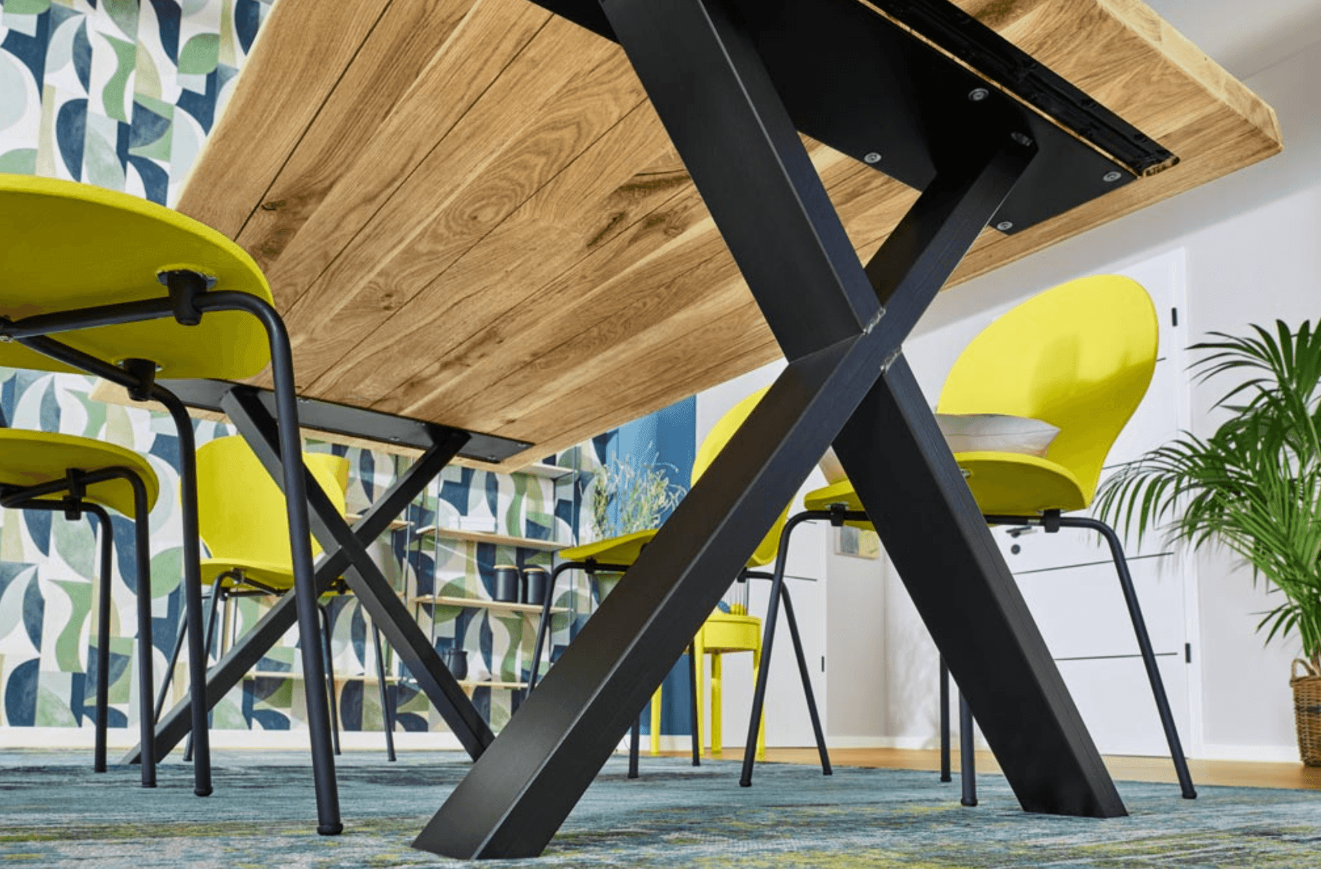 Modern dining area with a wooden table, yellow chairs, and patterned wallpaper.
